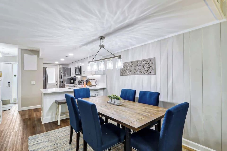 Modern dining area with blue upholstered chairs and a wooden table adjacent to a fully equipped kitchen.