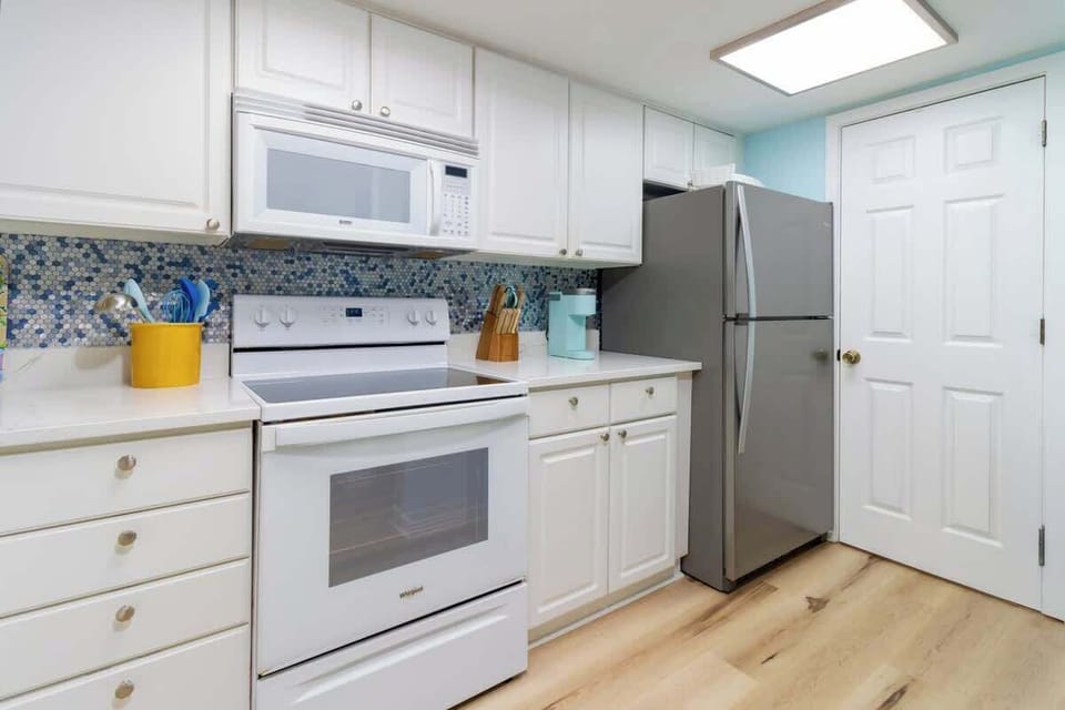 Modern kitchen with white cabinetry, stainless steel refrigerator, and blue mosaic tile backsplash