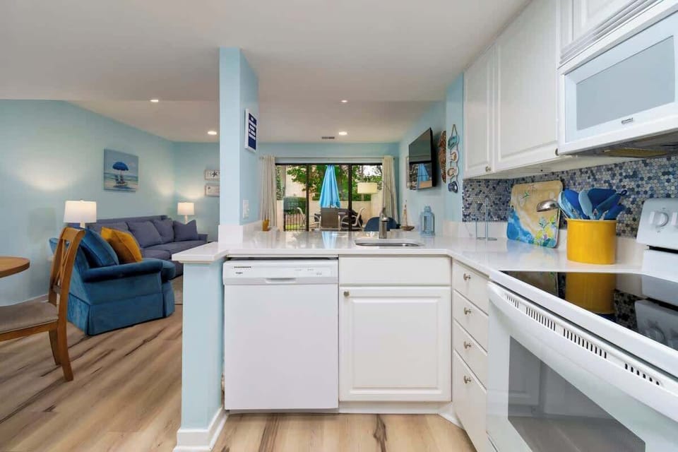 Bright kitchen with white cabinetry and a view into the cozy living area and outdoor patio.