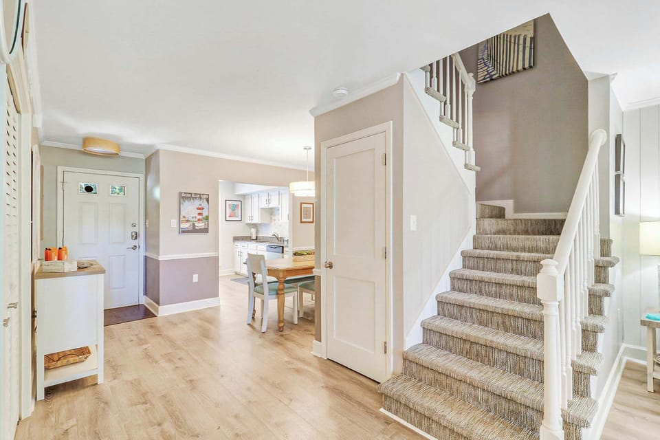 The open layout connects the entry, dining, and kitchen on the main level. The carpeted staircase with white railings leads to private upper-level bedrooms, giving guests their own retreat.
