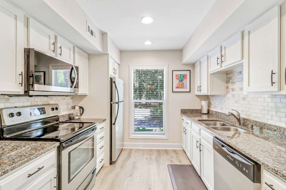 Cook in style with a full galley kitchen featuring white shaker cabinets, granite counters, marble tile backsplash, and stainless appliances including a range, microwave, fridge, and dishwasher.