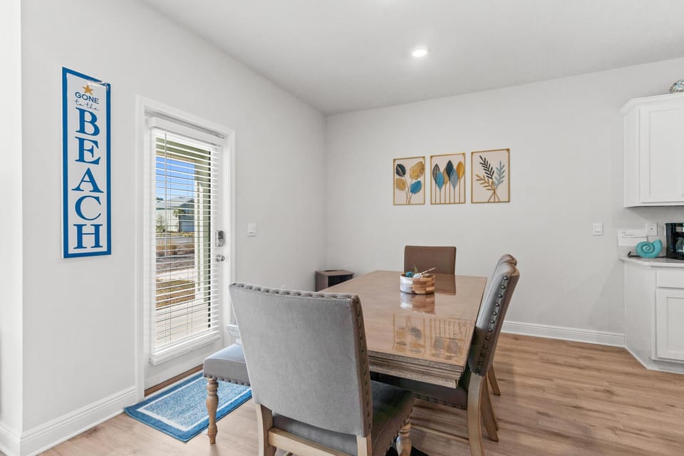 Gather around your bright dining table for memorable meals, surrounded by coastal charm and natural light streaming through the window.