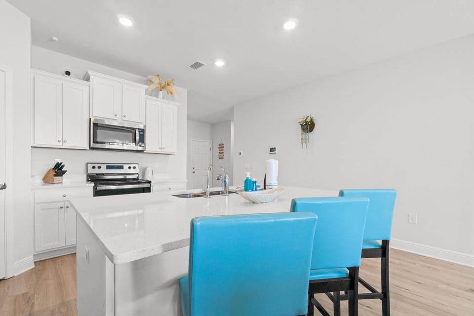 Your bright, modern kitchen features gleaming white cabinets, sleek countertops, and vibrant turquoise bar stools perfect for morning coffee or casual meals.