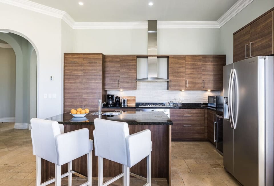 A modern kitchen with wood cabinets, black granite counters, stainless steel appliances, and a central island with bar seating.