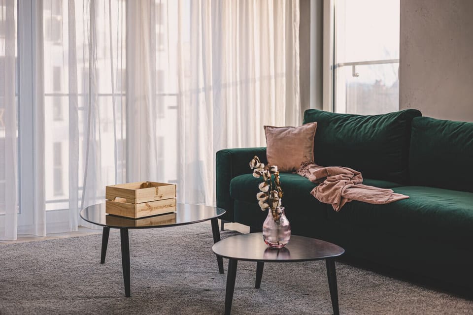 A stylish emerald-green sofa, perfect for unwinding after a day exploring the charms of Poznań`s Old Town. Sunlight streaming through the window adds warmth and coziness, creating a unique spot to relax with a view of the city.