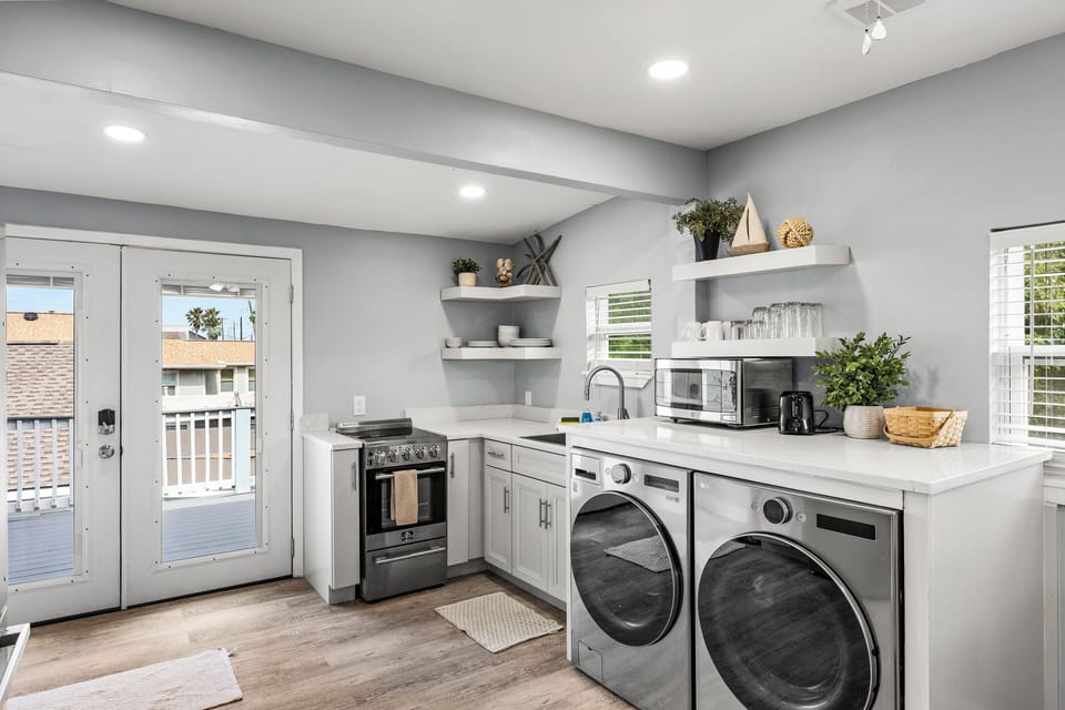 The kitchen at The Lookout at R½ opens directly to the wraparound deck via French doors — full range, in-unit washer and dryer, open shelving, and white countertops throughout.