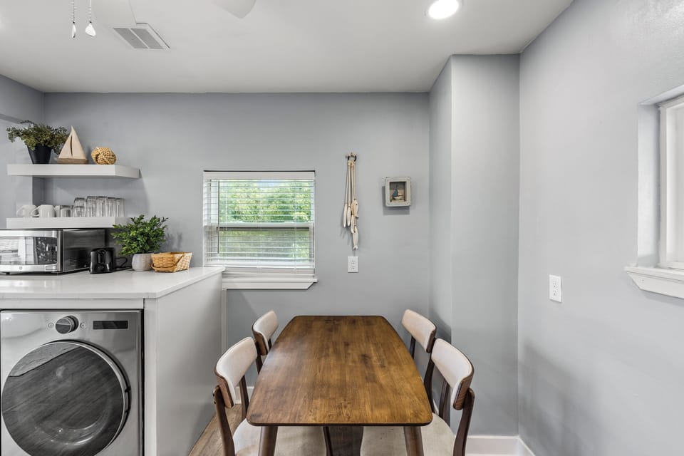 Dining area at The Lookout at R½ — a solid wood table for four, coffee station with open shelving, in-unit washer, and a bright window with neighborhood views.