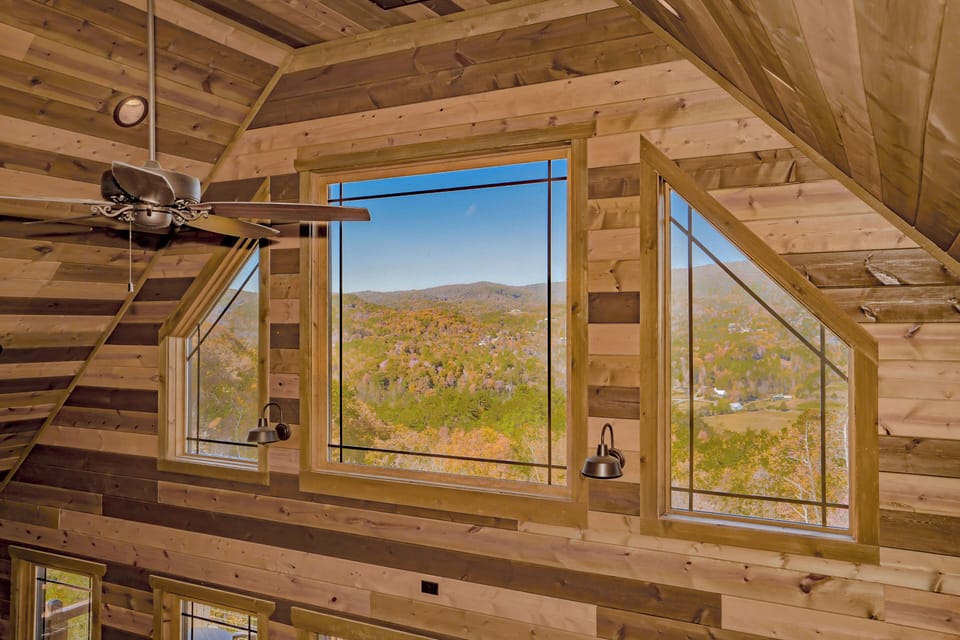 Rustic cabin interior with large windows showing autumn mountains outside.
