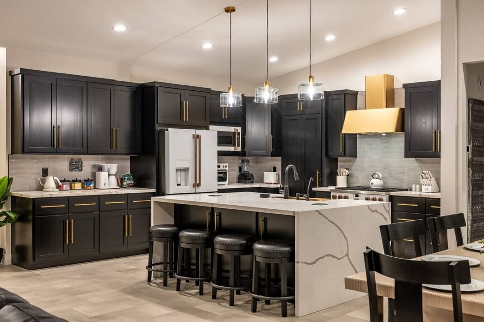 Luxury kitchen with gold accents, and a spacious island with bar seating. Features high-end appliances like a gas range, Café coffee maker, toaster oven, and Vitamix blender, perfect for cooking enthusiasts seeking elegance and functionality