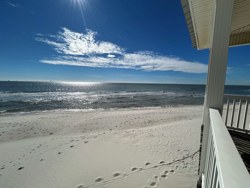 Stunning beachfront views from the property deck, featuring pristine white sand beach and sparkling ocean waves under brilliant blue skies.