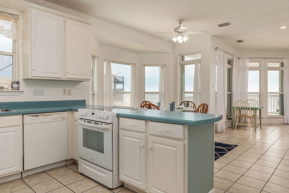 Your bright kitchen flows seamlessly into the dining area, with turquoise countertops and ocean views creating the perfect beachside cooking experience.