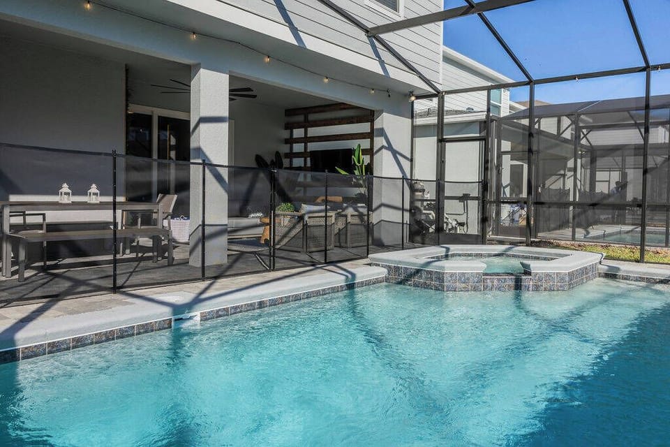 Step outside to enjoy a stunning private pool area featuring a sleek hot tub and modern lounge seating. The inviting blue water sparkles in the sun, and the screened enclosure guarantees comfort and relaxation during your stay.