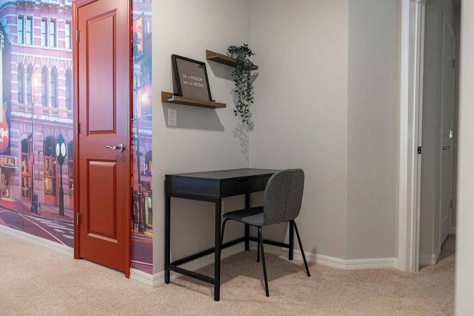 This cozy workspace offers a sleek black desk and a comfortable gray chair, ideal for catching up on emails or planning your day, while warm earthy tones and a vibrant mural create a welcoming atmosphere.