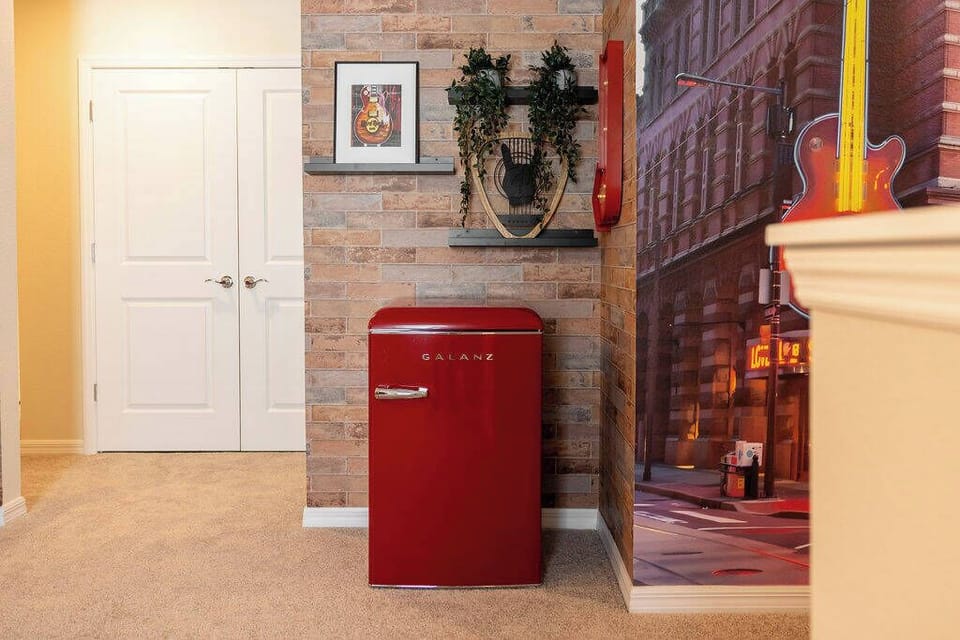 Experience a vibrant corridor with a charming retro red refrigerator that brightens the warm brick wall. Tasteful artwork and lush greenery create an inviting, homey atmosphere that makes you feel right at home.