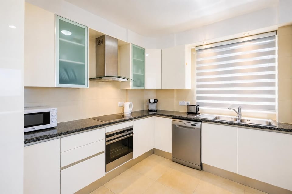 An interior view of the modern, L-shaped kitchen within the coastal house, featuring a clean white aesthetic and a highly functional layout.