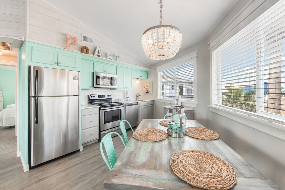 Your bright coastal kitchen features mint green cabinets, stainless steel appliances, and a crystal chandelier creating the perfect space for memorable meals.