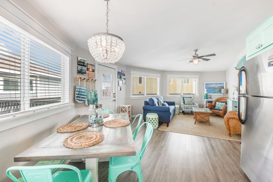 Step into your bright, coastal haven where natural light floods through elegant blinds, illuminating cheerful turquoise accents and comfortable seating.