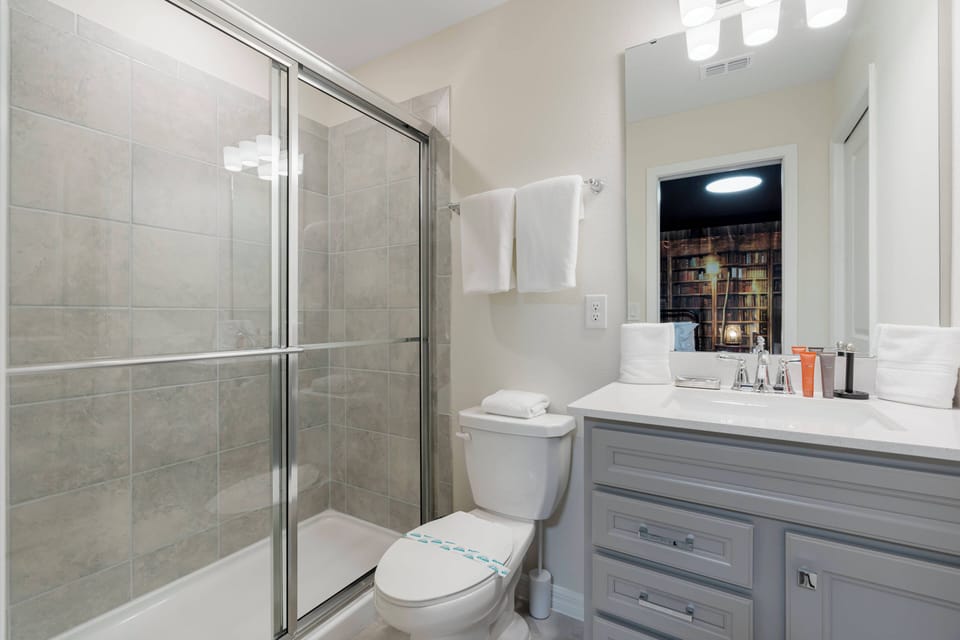 Step into a bright bathroom featuring a sleek glass shower and a stylish vanity with a light gray finish. The soft lighting above creates a warm atmosphere, while the organized shelves add a touch of convenience for your stay.