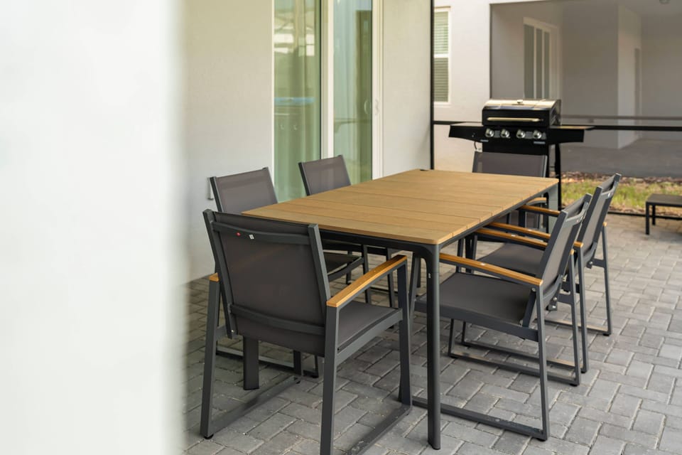 Gather around the sleek, wooden table surrounded by stylish, dark chairs—perfect for alfresco dining. The modern outdoor setting, complemented by a barbecue grill, invites lively meals and relaxed evenings under the stars.