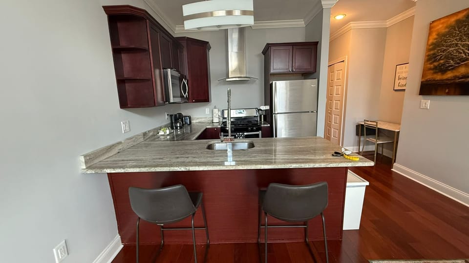 Fully-equipped kitchen with cherry wood cabinets, stainless appliances, granite counters, and high-top dining area that doubles as workspace ideal for preparing meals or remote work.
