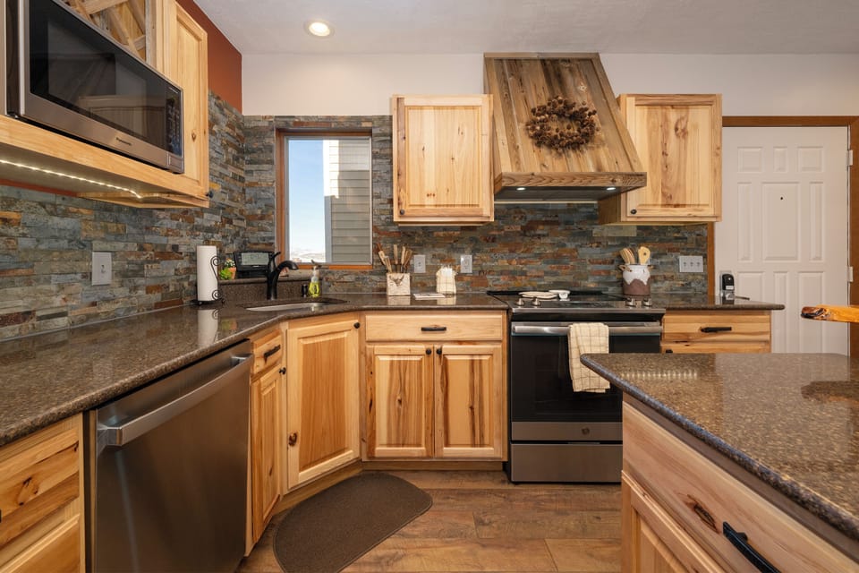 Your fully equipped kitchen at Mountainside B-20 features rustic wood cabinetry, granite countertops, and a striking stone backsplash for memorable mountain cooking.
