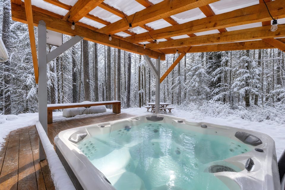 Hot tub beneath a wood pergola beside the snowy forest.