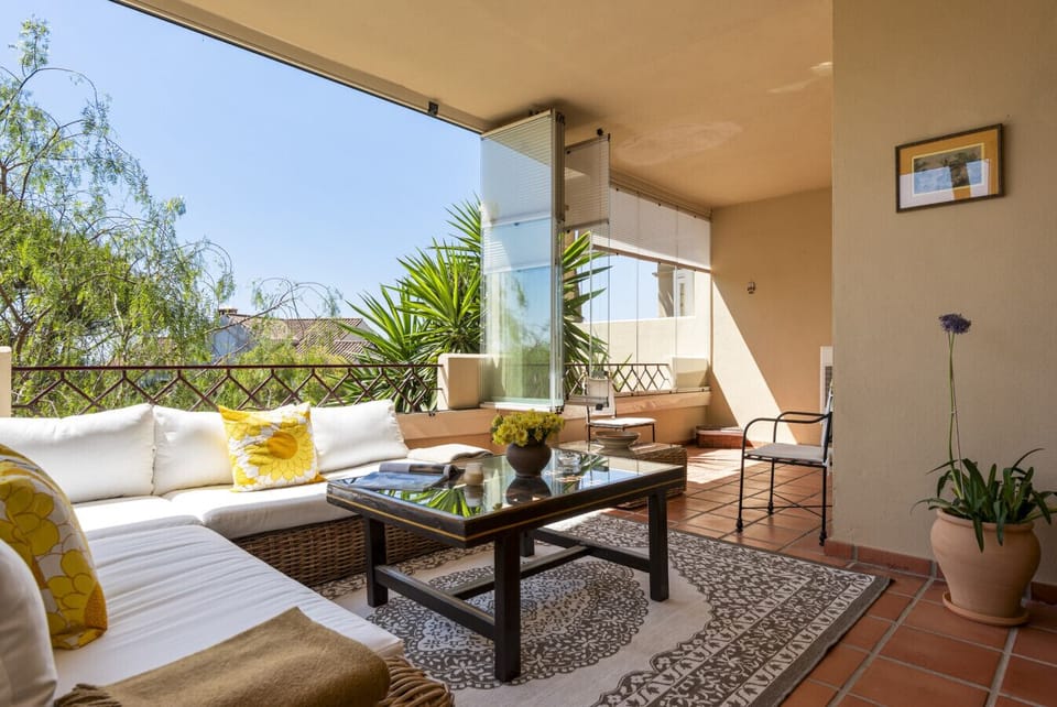 Sunny terrace with chillout seating area, dining area, Lumon glazing, and partial sea views