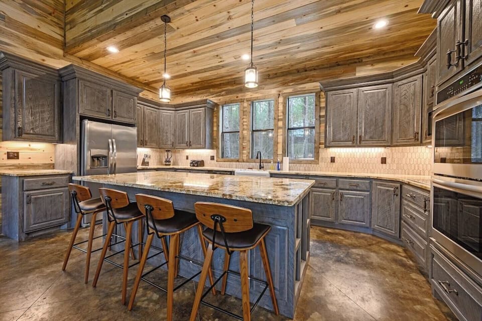 A rustic kitchen with granite countertops, stylish bar stools, and modern appliances makes cooking a delight. Perfect for a cabin getaway, this gourmet kitchen blends charm and convenience, ideal for a family-friendly retreat.