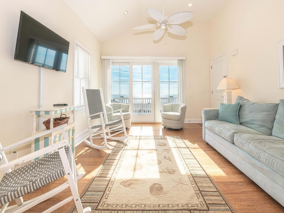 Relax in the bright living room featuring plush sofas, soft tones, and stunning ocean views through wide windows.