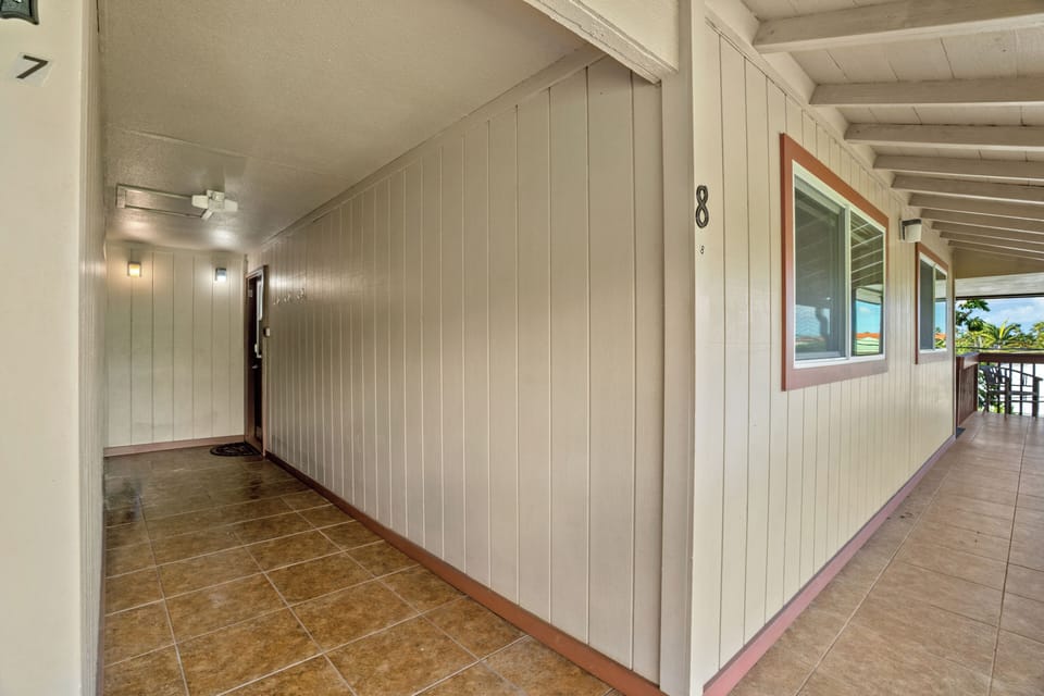 A covered exterior walkway connects unit 8 to unit 7, with glimpses of tropical greenery and distant views beyond. The property features clean, accessible corridors leading to each accommodation.