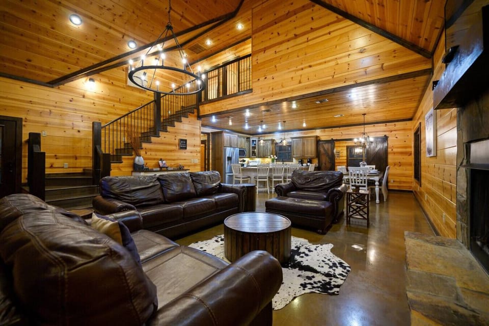 This massive open-concept living room with soaring wood ceilings, a statement chandelier, and leather seating arranged around a wood-slab coffee table is basically the ultimate hangout spot where everyone naturally gravitates.
