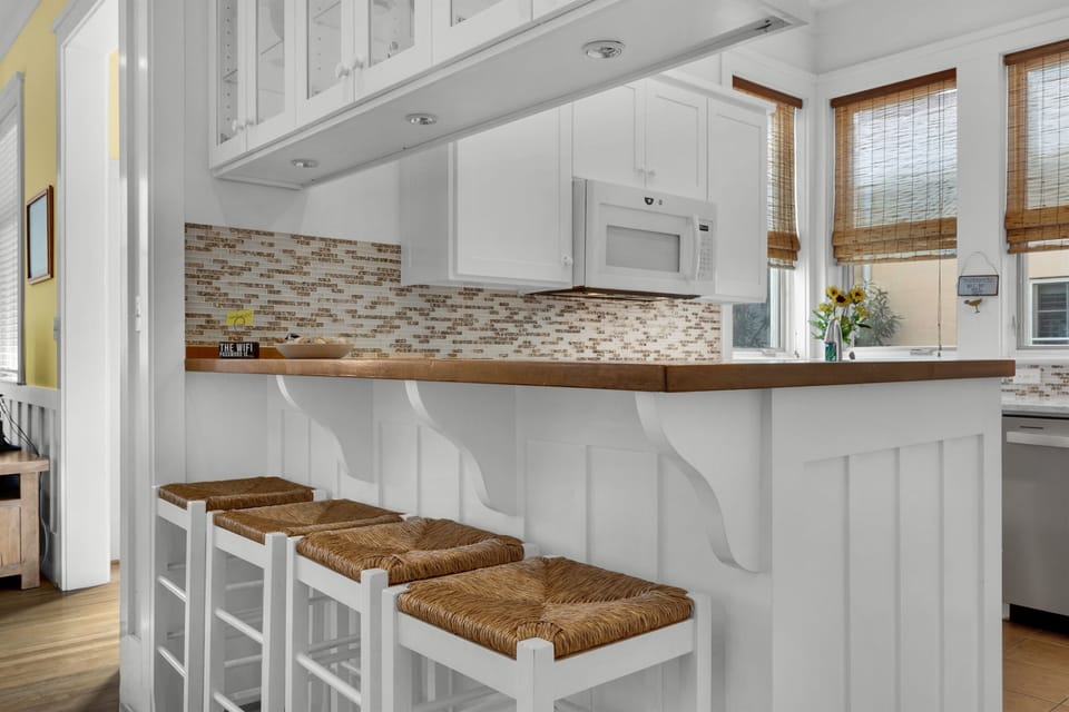 Your bright kitchen features white cabinetry, warm wood counters, and charming wicker bar stools perfect for morning coffee.