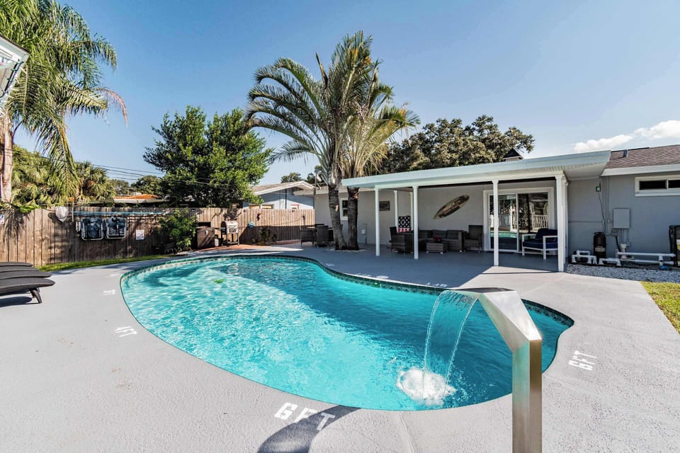 Luxury Largo pool home near Indian rocks Beach featuring custom heated pool with waterfall feature, expansive covered patio, and tropical palm landscaping. Private fenced yard perfect for Florida outdoor living and you pups 