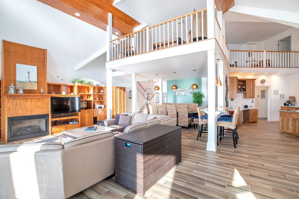 Spacious coastal living area with loft above, natural light, and comfortable seating