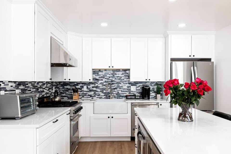 - Modern kitchen with bright white cabinets and stylish backsplash  
- Stainless steel appliances and farmhouse sink for easy cooking  
- Fresh roses add charm to the open kitchen and island design
