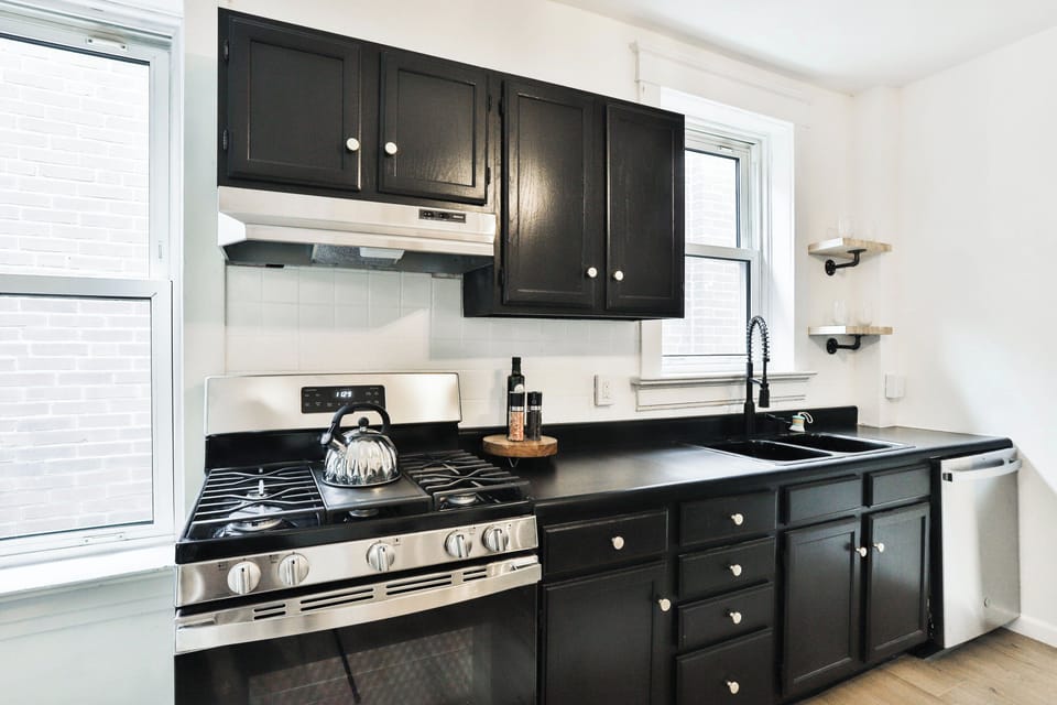 The kitchen workspace includes a gas range, black cabinetry and counters, double sink with spring faucet, windows, and dishwasher.