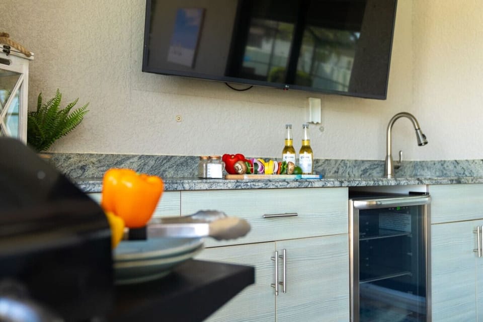 Cook, sip & watch the game in the covered outdoor kitchen with grill, sink, fridge & big-screen TV—perfect for breezy Florida evenings.