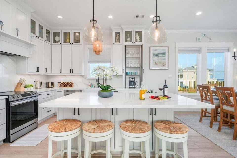 Bright coastal kitchen with oversized breakfast bar, open dining access, and premium finishes near ocean-view windows.