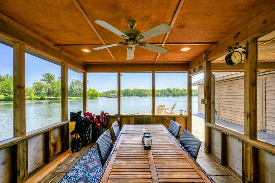 Screened-in area in the boathouse featuring a ceiling fan, comfortable seating, and a dining area with views of the lush green surroundings.