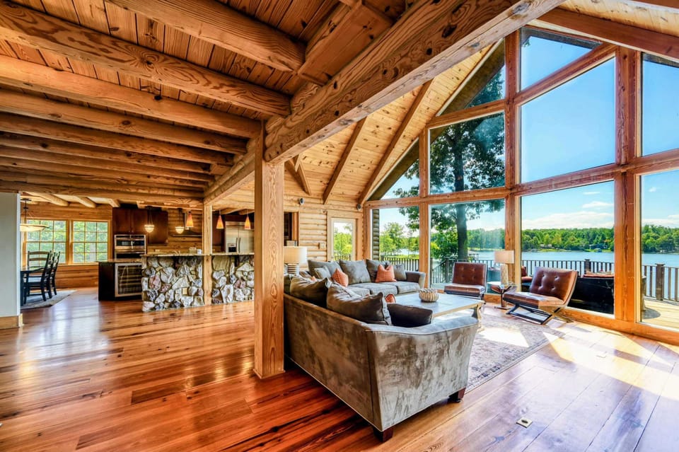 A warm and inviting open-concept living space features plush seating, vaulted wooden ceilings, and large windows with stunning lake views.