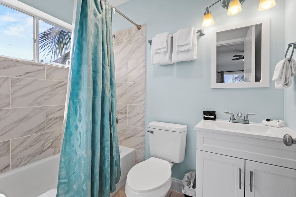 Ensuite bathroom features a shower tub with modern tile walls, white shaker vanity, and a toilet.