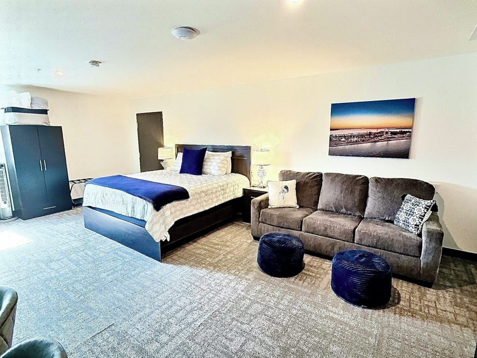 A bright, open room featuring a comfortable bed, work desk, ample storage, and a large TV, perfect for relaxing or working during your stay.