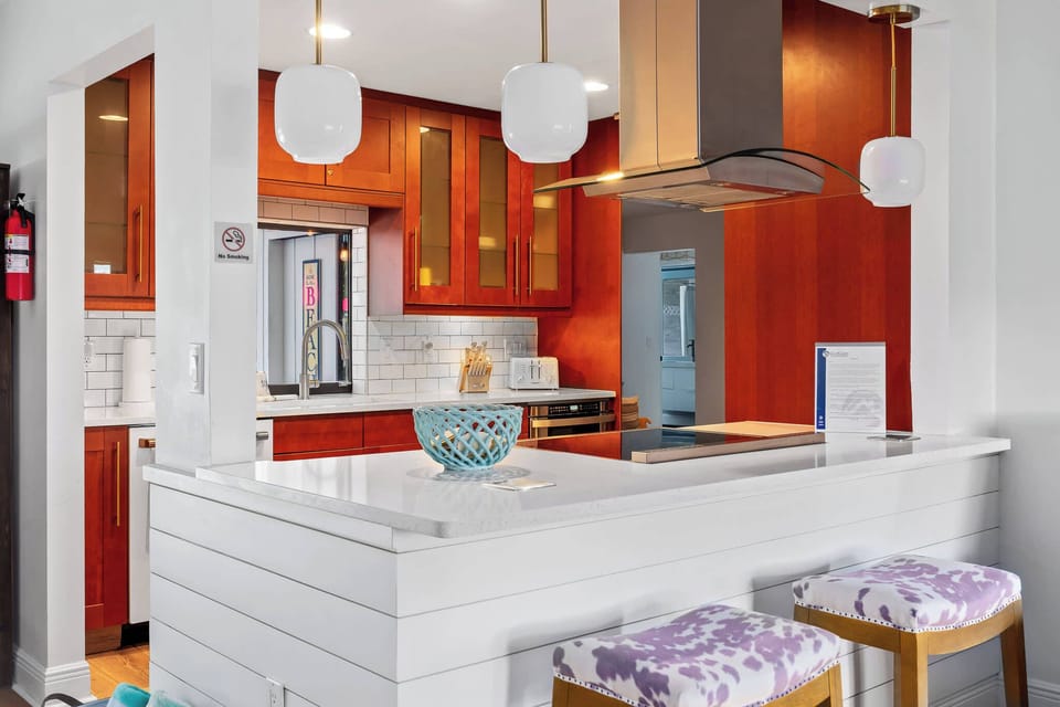 This image features a modern kitchen bar with a white quartz countertop and sleek wooden cabinets. Three stylish pendant lights hang above, illuminating a decorative blue bowl. 
