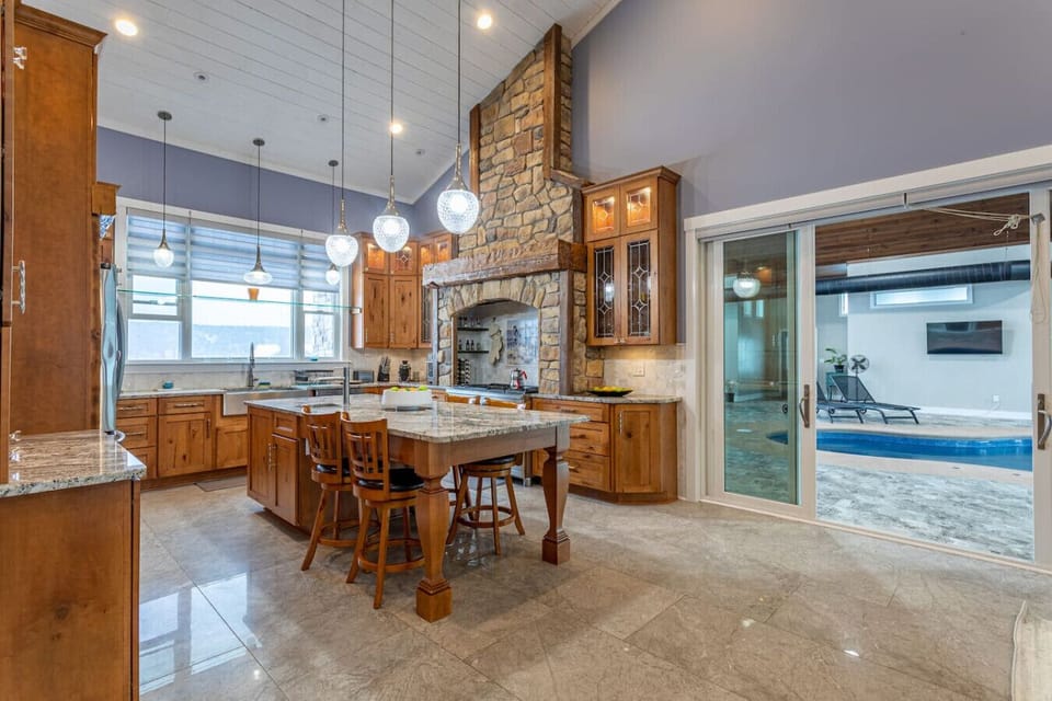 Kitchen wide angle showing island seating, stone range hood, and sliding doors open to the pool room