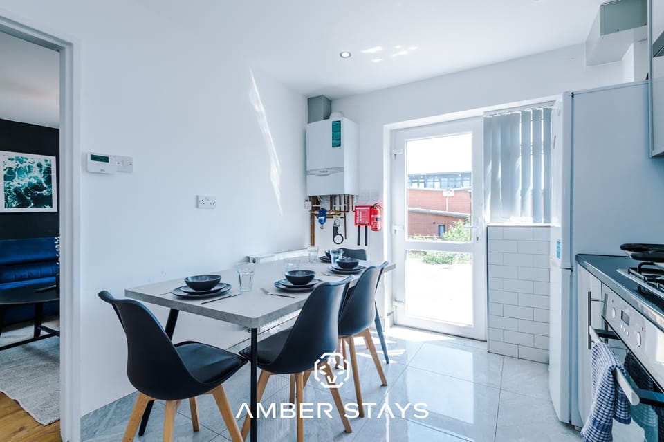 This modern dining area is perfectly situated within the kitchen, creating a bright and social heart for the home. It features a sleek, grey dining table paired with four stylish black chairs with wooden legs, offering a clean and contemporary look.