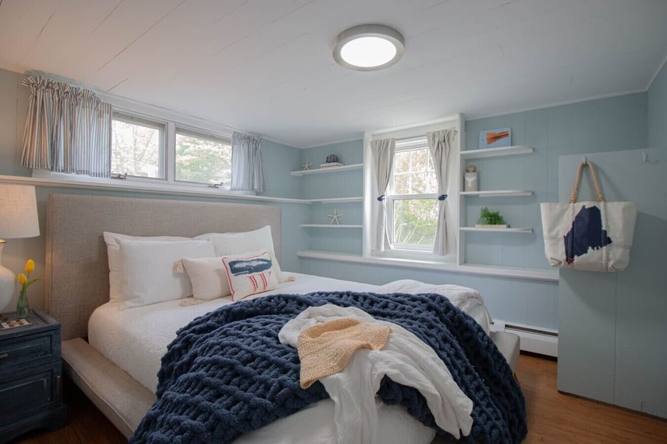 This cozy bedroom is bright and charming, featuring a small closet for hanging clothes, shelving for additional storage, and a full-length mirror.