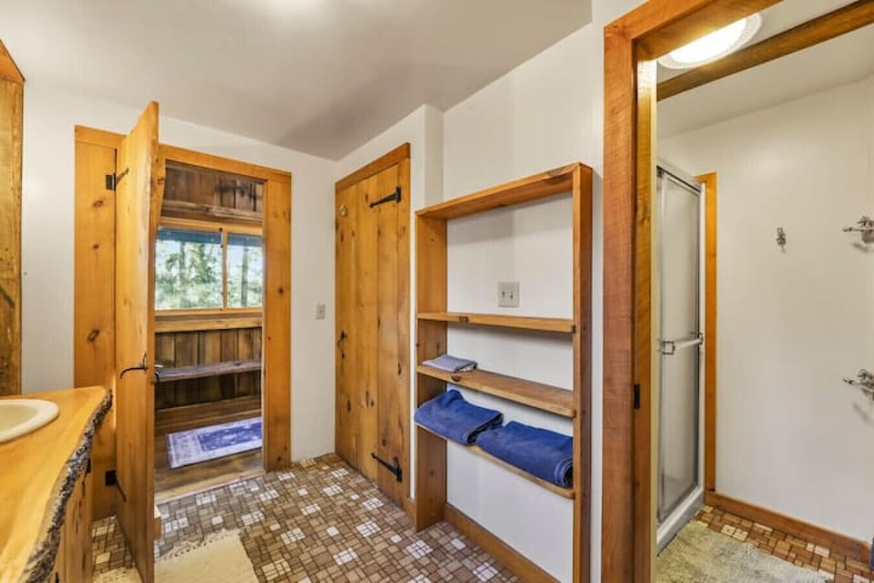 A rustic hallway leading into the bathroom, with open shelving for towels and essentials, featuring natural wood trim and doors.