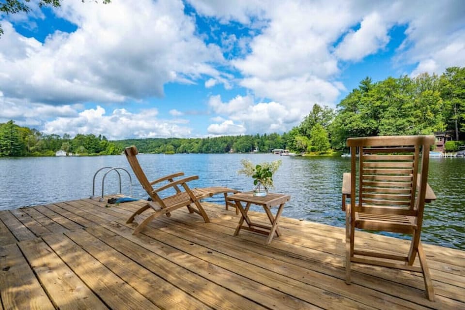 A spacious wooden dock with lounge chairs and a ladder for lake access, offering panoramic water views and a peaceful place to relax.