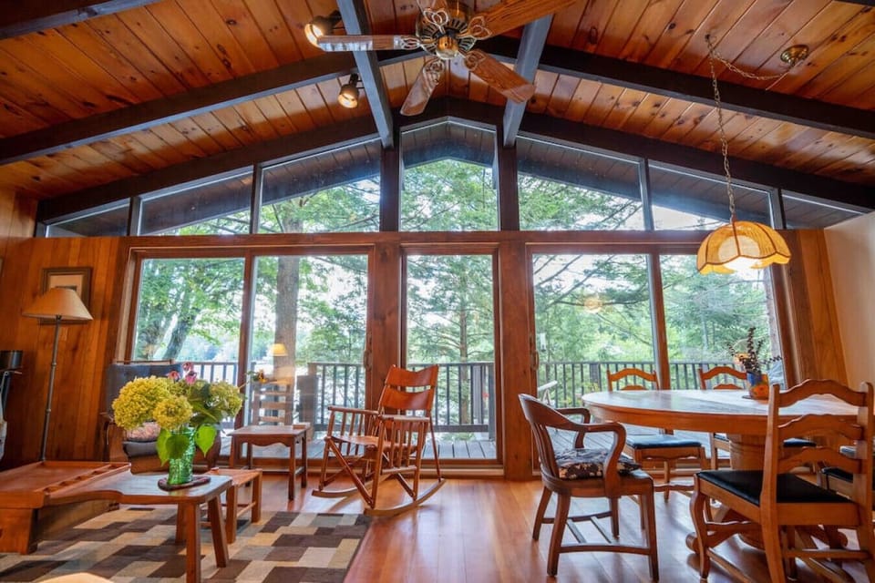 A warm, wood-paneled dining space with large windows, and a rustic table set for six, perfect for meals with a view.