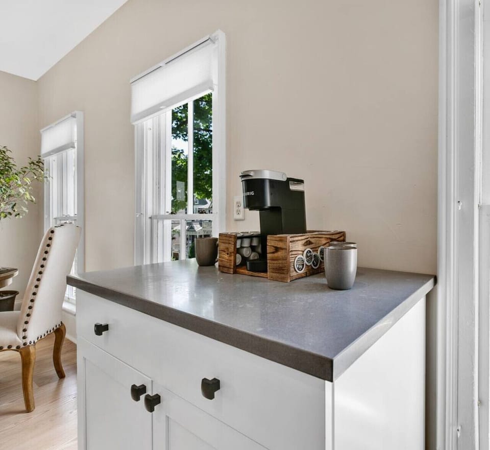 Cute coffee bar setup with a Keurig, mugs, and small storage baskets near a window.